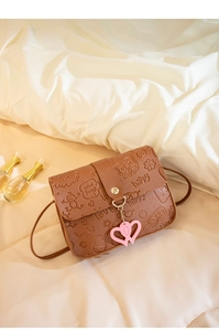 Close-up of brown embossed crossbody bag with pink heart pendant and gold buckle detail