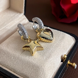 Asymmetric gold and silver tone earrings with star and heart charms on black velvet