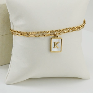 Primer plano de la pulsera dorada de doble capa con colgante de letra K y nácar blanco