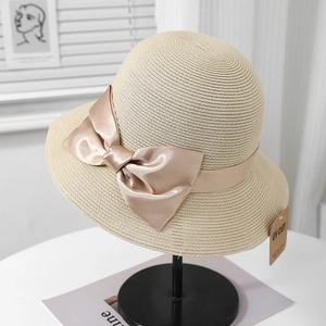 Détail d'un chapeau de paille beige avec nœud en satin champagne et étiquette anti-UV