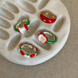 Detail of creative apple-themed enamel adjustable rings on a beige ceramic tray