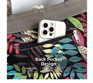 Close-up of the back zipper pocket on a tropical leaf print canvas tote bag with a phone