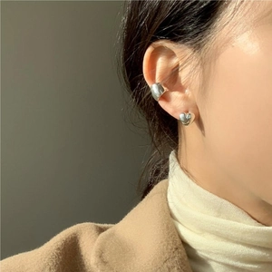 Close-up of heart stud and wide silver cuff worn on the ear in minimalist style
