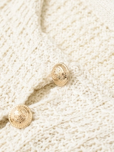 Macro detail of cream knit sweater texture with ornate gold embossed metal button