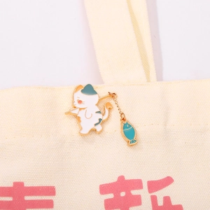 Cute white cartoon cat enamel brooch with dangling blue-green fish on canvas bag