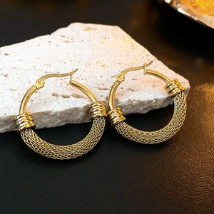 Detailed macro view of gold-tone braided texture hoop earrings on white stone base