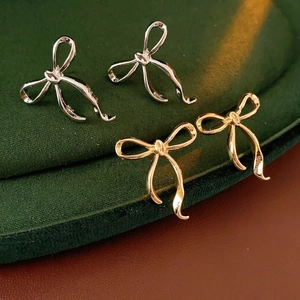 Elegant bow-shaped stud earrings in gold and silver finish on luxury velvet display