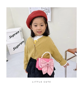Detail of pink tweed girl's crossbody bag with pearl handle and bow decoration