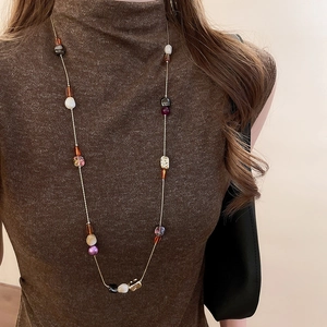 Détail de perles en résine colorées sur une longue chaîne dorée et pull marron