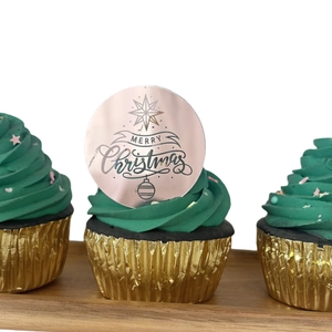 Close-up of rose gold acrylic Merry Christmas cupcake topper on green frosting
