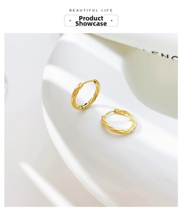 Macro side view of gold twisted rope hoop earrings with minimalist texture on white prop