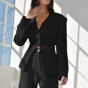 Detail of black cropped blazer with waist cutout design and matching wide-leg trousers