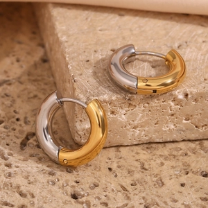 Macro detail of two-tone gold and silver stainless steel C-shaped earrings on stone