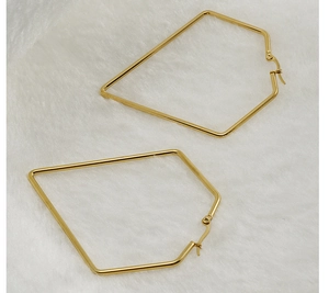 Detail of golden geometric polygonal hoop earrings on a soft white textured background
