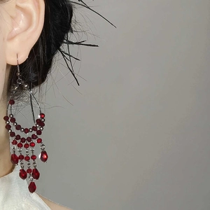 Close-up of red beaded tassel earrings with silver hooks shown on a female model