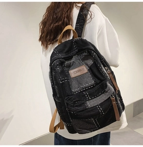 Close-up of black denim backpack with white stitching and leather handles on person