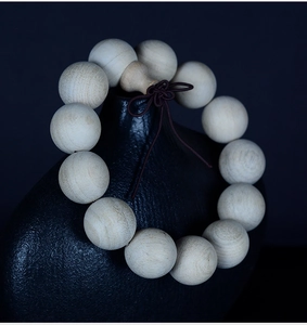 Detailed close-up of natural camphor wood beads showing wood grain on a black vase