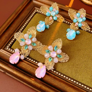 Macro view of vintage gold wire flower earrings with colorful gems in a wooden tray