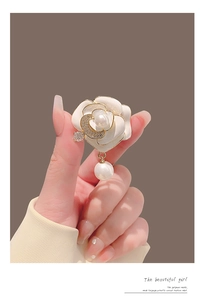 Détail d'une broche camélia avec pétales en émail blanc, perles et accents dorés
