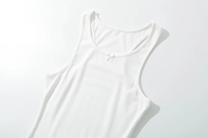 Close-up detail of white ribbed tank top featuring a delicate ribbon bow on the neckline