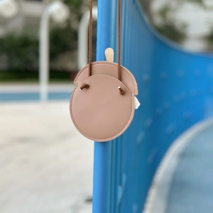 Close-up of pink leather acorn-shaped kid's crossbody bag hanging on a blue fence
