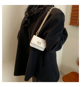 Detailed view of white quilted crossbody bag with gold chain and twist lock on black suit