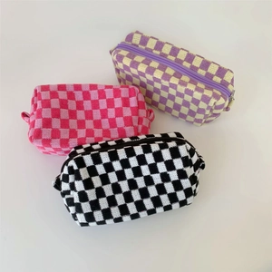 Three knit checkerboard cosmetic bags in pink, purple, and black on a white background