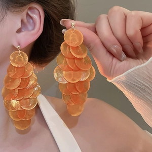 Detail of layered orange shell tassel earrings worn by a model for a beach vacation style