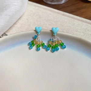 Detail of heart-shaped blue stud earrings with colorful bead tassels on ceramic plate