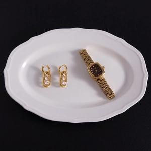 Dettaglio di orecchini in oro 18k con zirconi marquise e orologio a catena nero quadrato