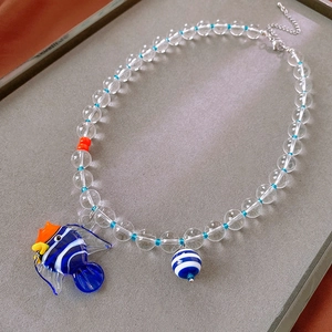 Macro view of transparent beaded necklace with blue tropical fish pendant on grey tray