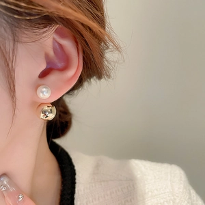 Detail view of gold-plated double-sided earrings with white pearl and metal ball on ear