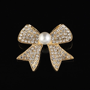 Élégante broche nœud dorée sertie de cristaux et perle blanche sur fond noir profond