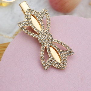 Close-up of golden bow-shaped hair clip with shimmering rhinestones and pearl details