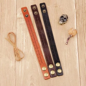 Detailed shot of leather bracelets with ruler markings and engraved text on wood