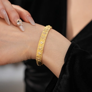 Detail of gold-plated bangle featuring a brushed metal texture and zircon flower cluster