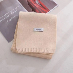 Detail of folded beige knitted scarf featuring a minimalist stitched FEIDING brand label