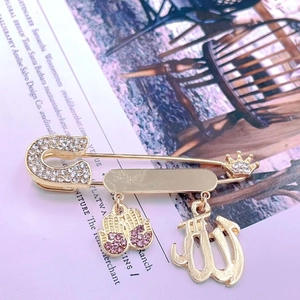 Close-up of golden safety pin brooch with sparkling crystals and Arabic crown pendant