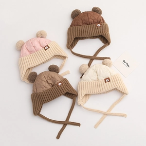 Detail von vier bunten Kinder-Strickmützen mit Plüschpompons und Steppmuster