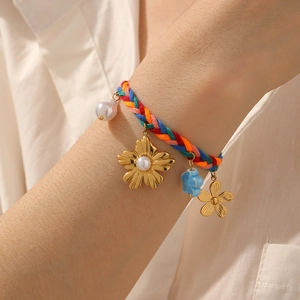 Detailed view of colorful woven cord bracelet with gold floral and pearl charms on wrist