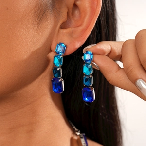 Close-up of dangling geometric earrings with blue rectangular crystals and metal settings