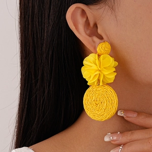 Detail of yellow raffia woven flower earrings in a bohemian three-tier drop design