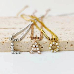 Primer plano de collares de letras dorados y plateados con perlas sobre piedra
