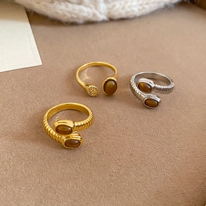 Detailed view of adjustable gold and silver rings with oval tiger eye stones on beige fabric