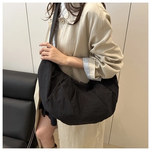 Detailed view of black nylon crescent shoulder bag on beige trench coat outfit