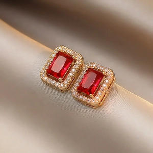 Macro shot of gold square stud earrings with emerald-cut red stone and white zircon halo