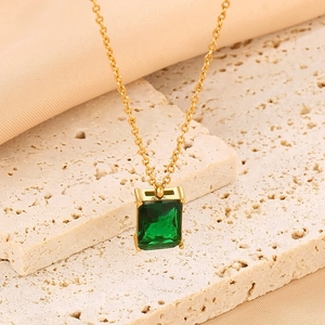 Detail of a square emerald glass pendant on a gold titanium steel chain on stone