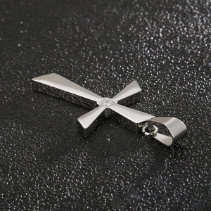 Macro view of polished silver cross pendant with a single diamond inlay on a dark texture