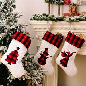 Drei weiße gesteppte Nikolausstiefel mit rot-schwarzem Karomuster hängen an einem Kamin