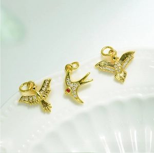 Detail of 18K gold plated bird charms with micro-paved zircons on a white ceramic tray